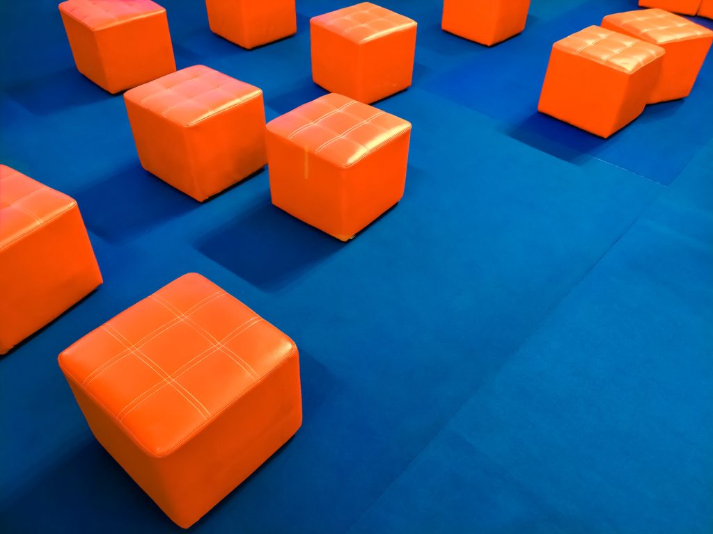 Many orange cubic padded stool chairs on blue carpet in event stage area in shopping mall